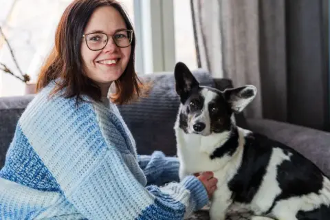 Kvinna med glasögon och en hund med finska hundnamn sitter i en soffa.