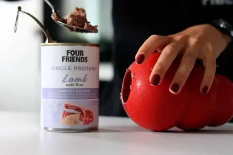 En burk med Four Friends Single Protein Lamm med ris, perfekt protein hundmat. En sked med mat lyfts ur burken, bredvid en röd leksak.