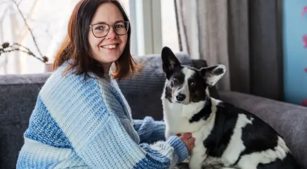 Kvinna med glasögon och en hund med finska hundnamn sitter i en soffa.