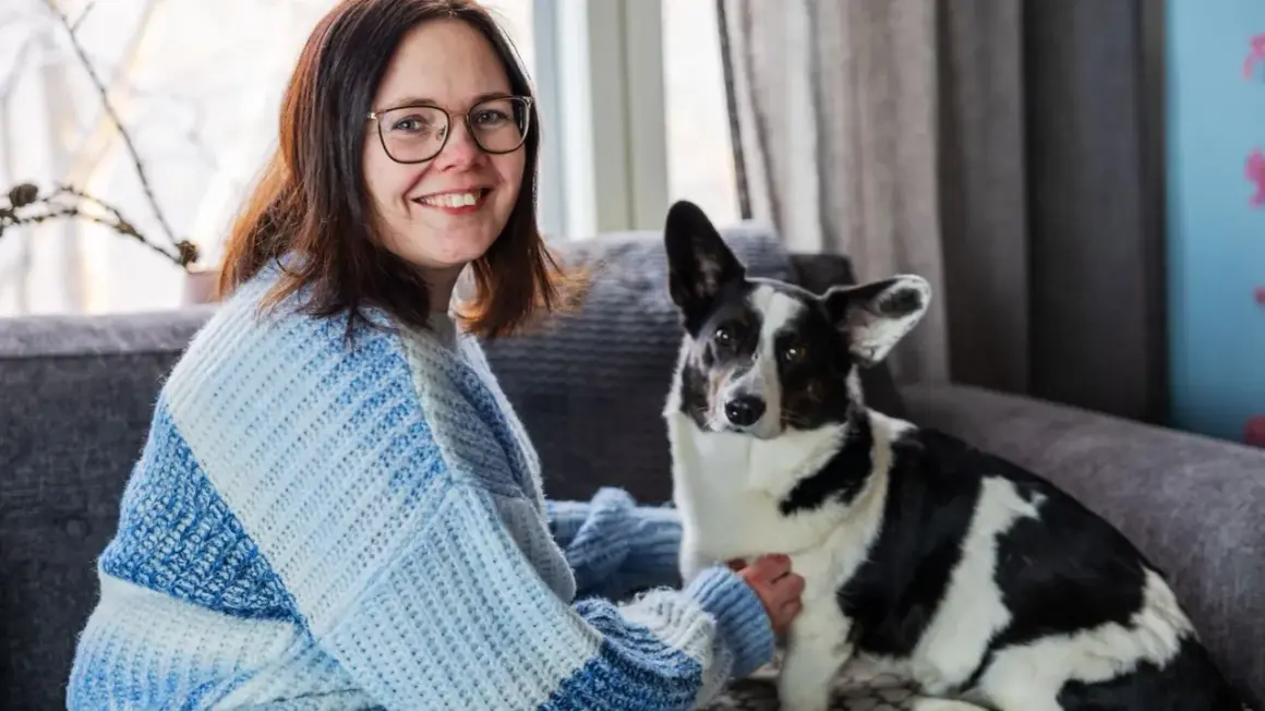 Kvinna med glasögon och en hund med finska hundnamn sitter i en soffa.